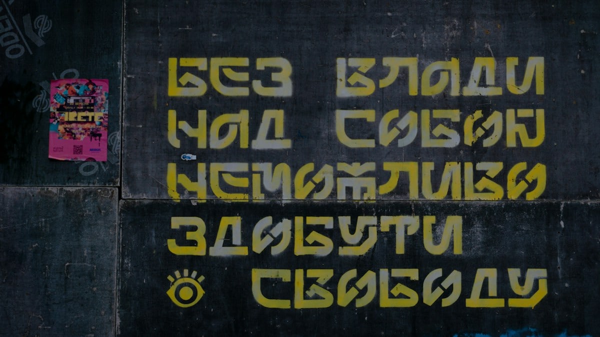 a black wall with yellow and pink graffiti on it